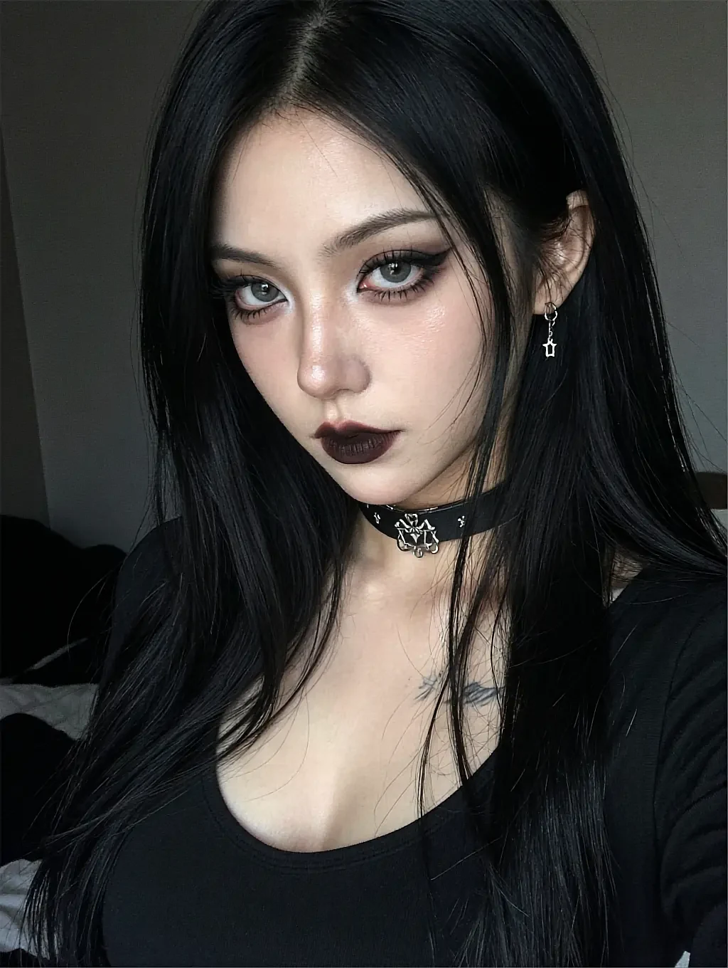 Dark-haired woman with dark lipstick and studded choker with star earring in a black top in a bedroom